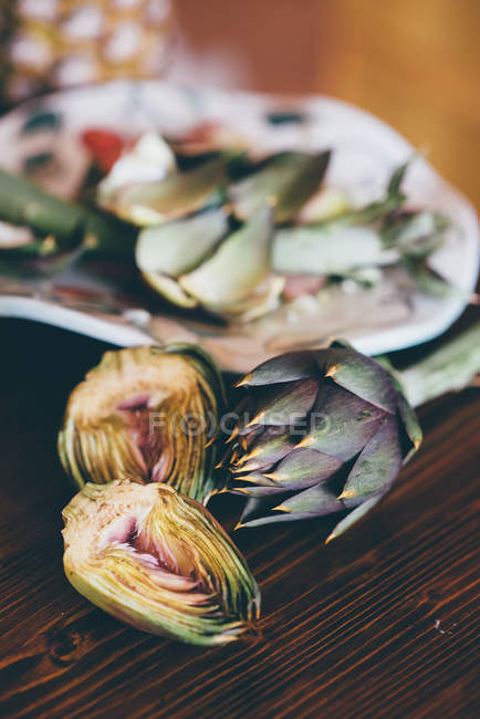 Metade e alcachofras globo inteiro na mesa da cozinha — Fotografia de Stock