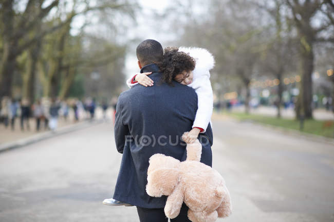 Vista posteriore del padre che porta la figlia addormentata che tiene il giocattolo coccoloso — Foto stock