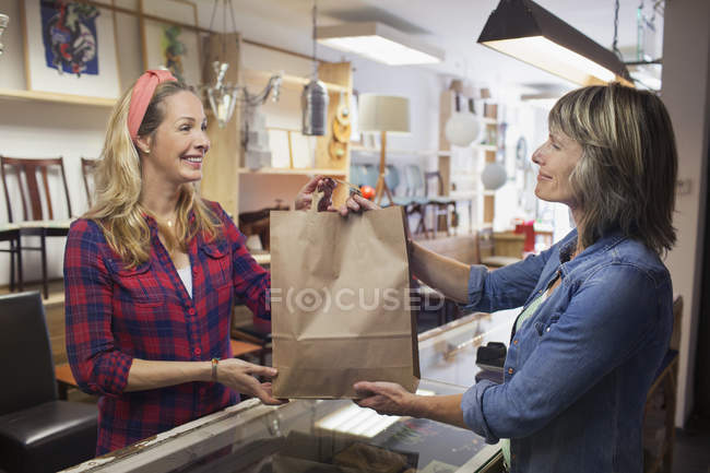 Assistente de loja entregando saco de compras comprador — Fotografia de Stock