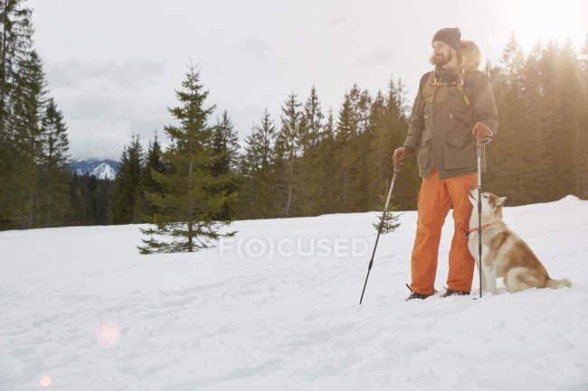 Взрослый мужчина в снежной обуви, собака рядом с ним, Эльмау, Бавария, Германия — стоковое фото