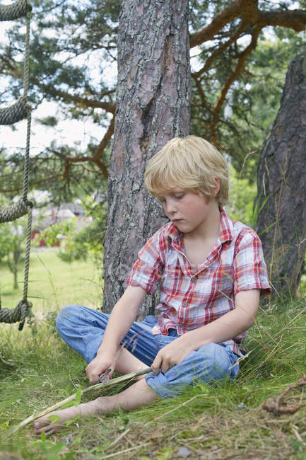 Jeune garçon nettoyage branche d'arbre avec couteau — Photo de stock