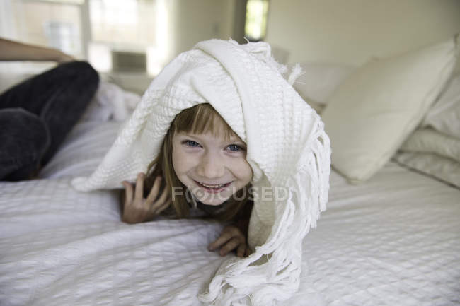 Jeune fille regardant la tête hors de sous couverture sur le lit — Photo de stock