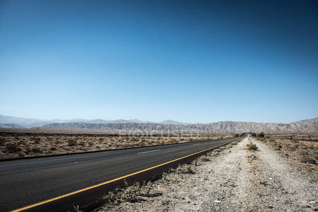 Road stretching to mountain range under clear blue sky — Stock Photo