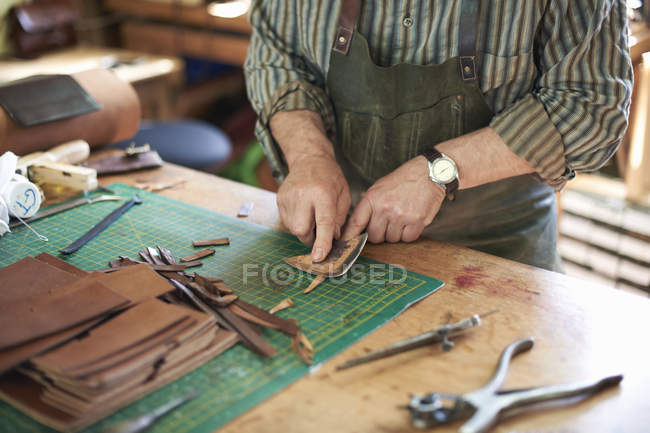 Чоловік-працівник у шкіряній майстерні, перевірка гостроти ножа на шкірі, середня секція — стокове фото