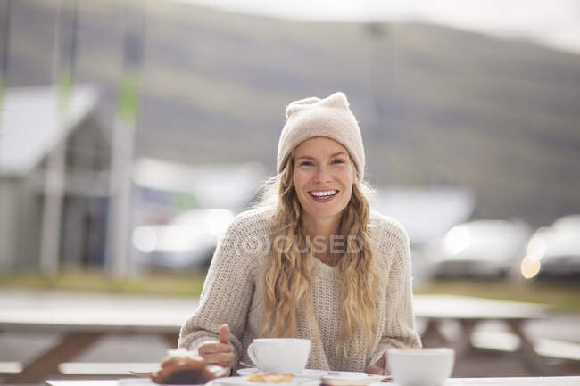 Porträt einer Touristin mit Strickmütze beim Kaffee auf einer Picknickbank, Seyoisfjorour, Island — Stockfoto