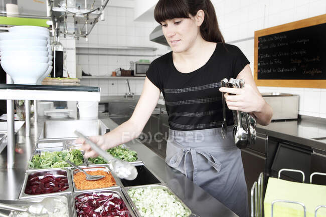 Donna che lavora in cucina ristorante, tenendo pinze per insalata — Foto stock