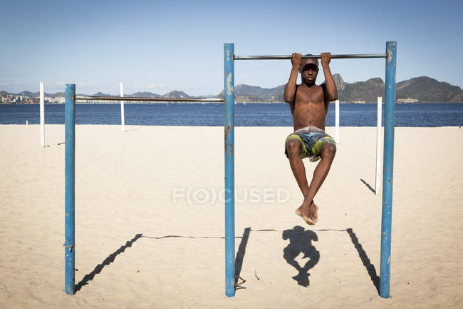 Young man doing chin ups on beach — Stock Photo