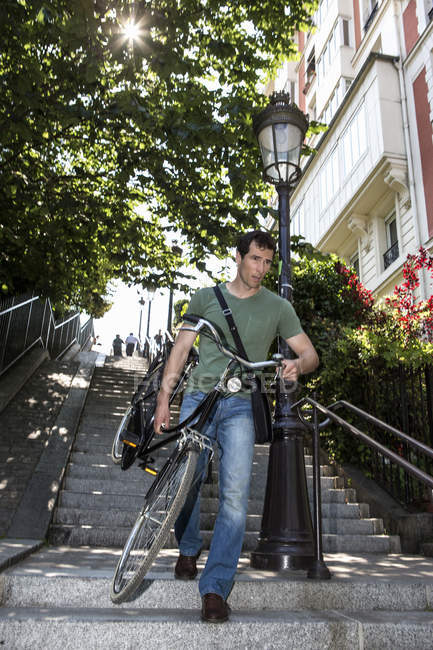 Homme mi-adulte transportant un vélo dans un escalier à Paris, France — Photo de stock