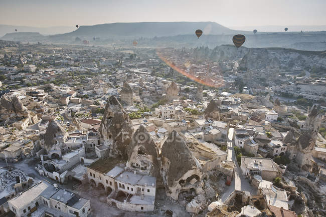 Возвышенный вид воздушных шаров над скалами и жилищами, Каппадокия, Анатолия, Турция — стоковое фото
