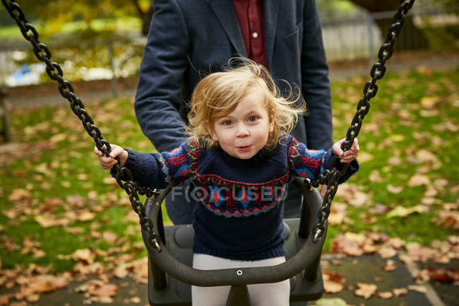 Father pushing daughter on playground swing — Stock Photo