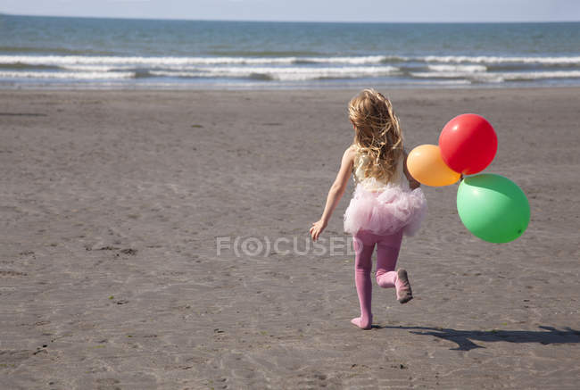 Fille sur la plage portant tutu tenant des ballons, Pays de Galles, Royaume-Uni — Photo de stock