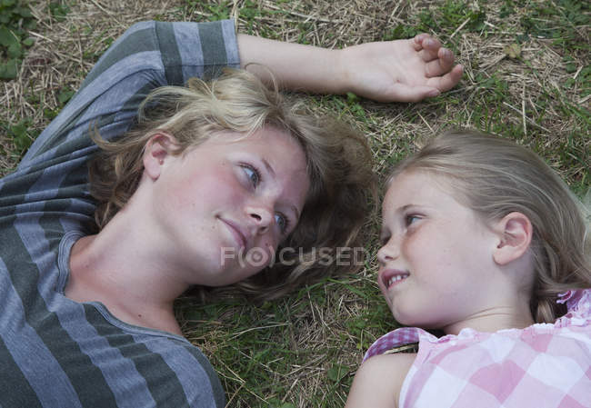 Hermanas tumbadas en la hierba, cara a cara - foto de stock