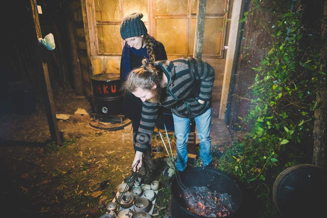 Casal usando pinças para remover panelas de barro do fogo, sorrindo — Fotografia de Stock