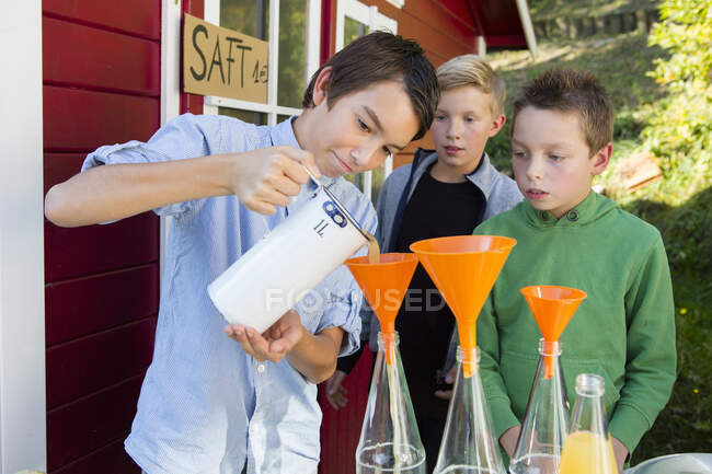 Мальчик-подросток и братья наливают свежий апельсиновый сок на продажу на обочине дороги — стоковое фото