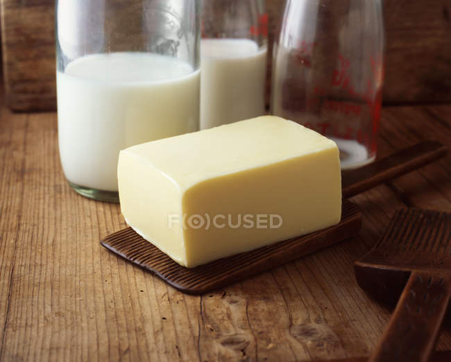 Блок масла с молочными бутылками на деревянном столе — стоковое фото