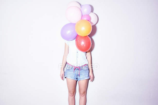 Студийный снимок молодой женщины, стоящей за кучей воздушных шаров — стоковое фото