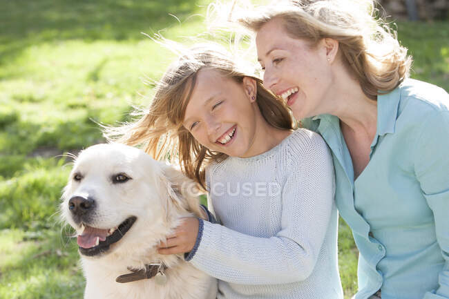 Madre e hija en el jardín con perro sonriendo - foto de stock