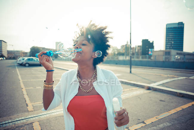 Young woman blowing bubbles in city parking lot — Stock Photo