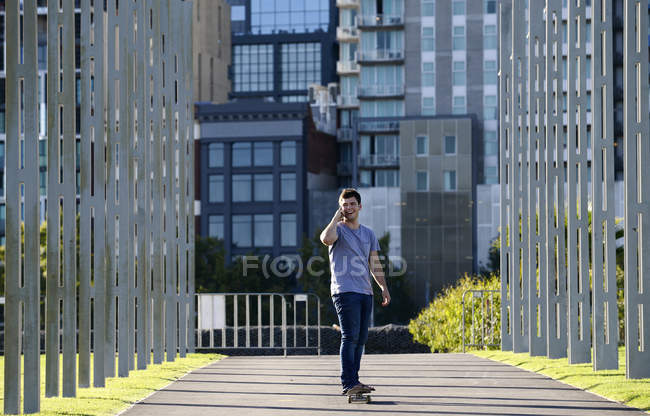 Молодой человек на скейтборде, используя мобильный телефон — стоковое фото