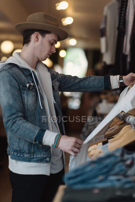 Jeune homme regardant les vêtements dans le magasin de vêtements — Photo de stock