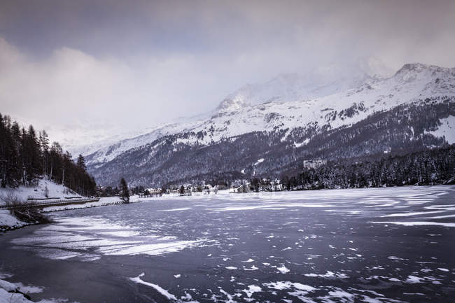 Lago e villaggio ghiacciato sotto la montagna innevata, Engadina, Svizzera — Foto stock