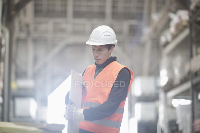 Jovem trabalhador armazém examinando prancha no armazém — Fotografia de Stock