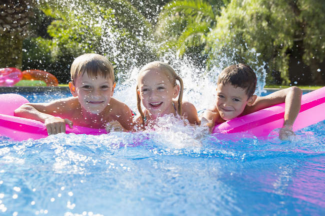 Portrait de trois enfants éclaboussant sur matelas gonflable dans la piscine du jardin — Photo de stock