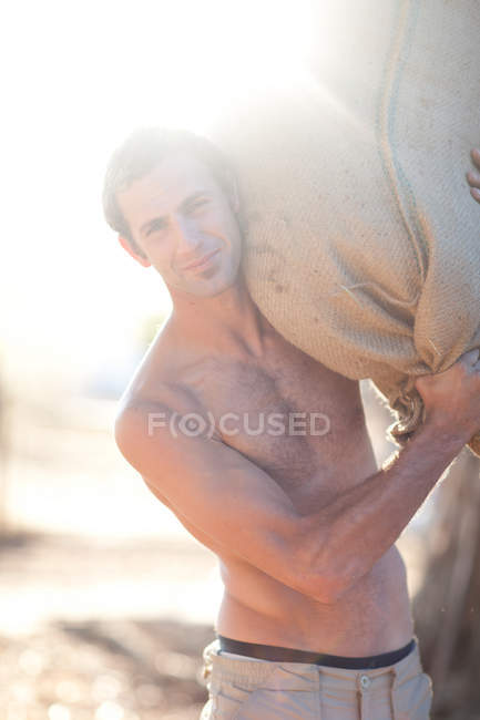 Young man carrying heavy sack — Stock Photo