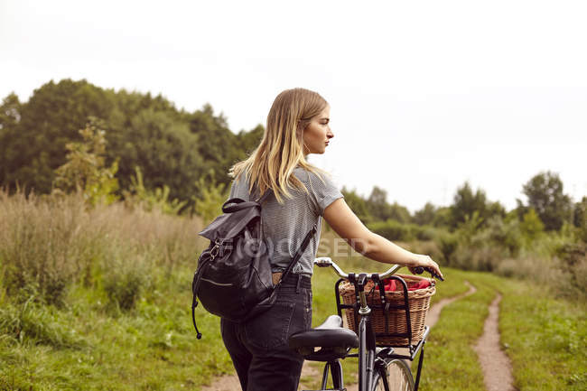 Mujer joven con bicicleta mirando por encima de su hombro desde la pista de tierra rural - foto de stock