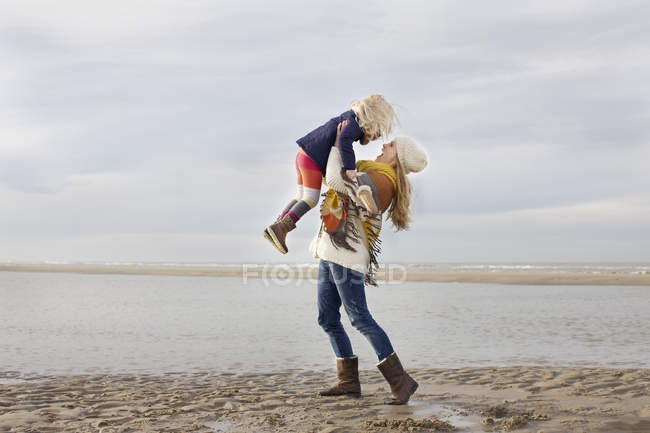 Mulher adulta média levantando filha na praia, Bloemendaal aan Zee, Países Baixos — Fotografia de Stock