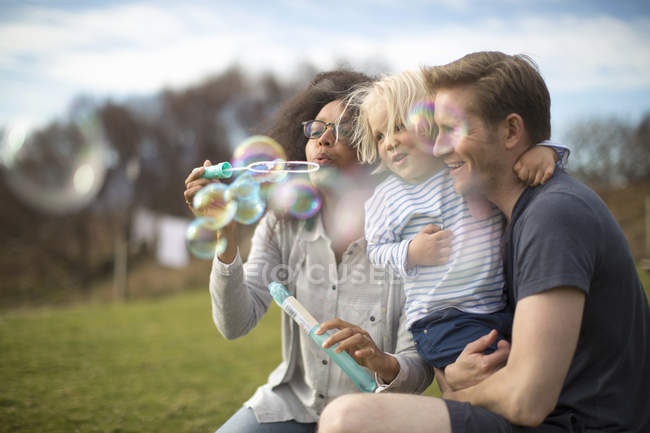Mother blowing bubbles, father holding son — Stock Photo