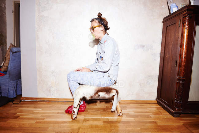 Junge Frau sitzt auf Hassock mit Sonnenbrille und pustet Kaugummi — Stockfoto