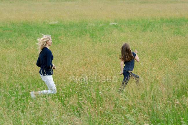 Мать и дочь бегут через длинное травяное поле — стоковое фото