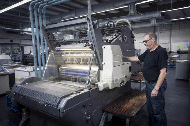 Worker operating print machine in printing workshop — Stock Photo
