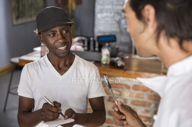 Employee in restaurant talking with chef, making notes in notebook — Stock Photo
