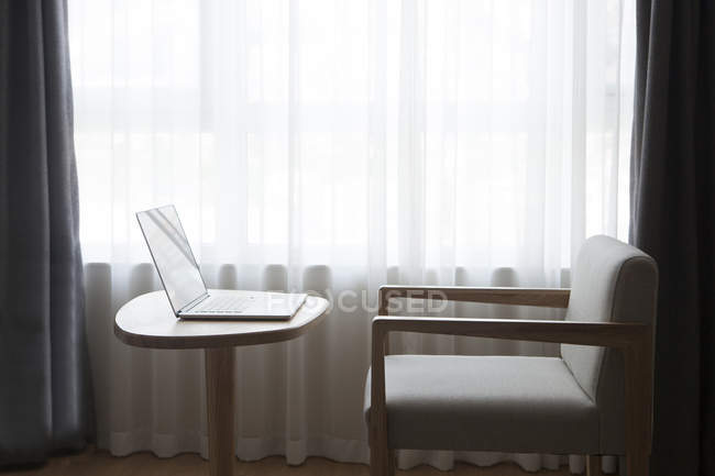 Ноутбук на столе со стулом, перед окном — стоковое фото