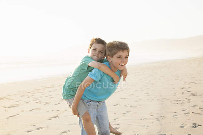 Хлопчик дає братові скарбничку на пляжі — стокове фото