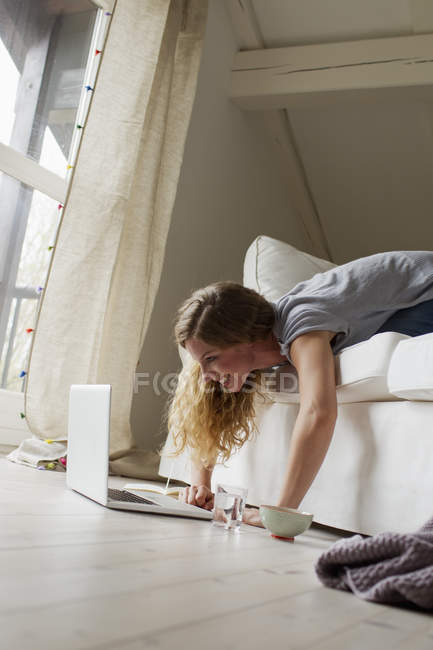 Жінка лежить на дивані за допомогою ноутбука — стокове фото