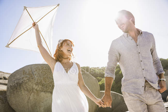 Low angle view of couple holding hands, holding kite face to face smiling — Stock Photo