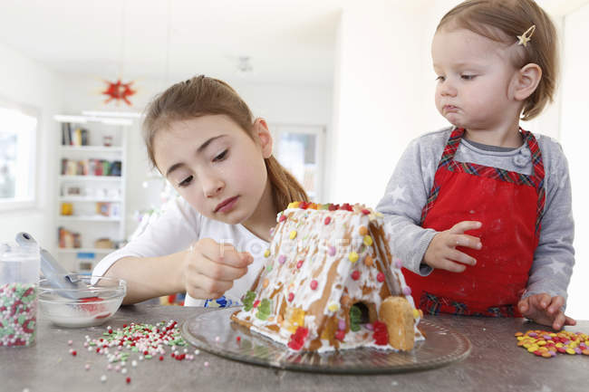 Sisters at kitchen counter decorating ginger bread house — Stock Photo