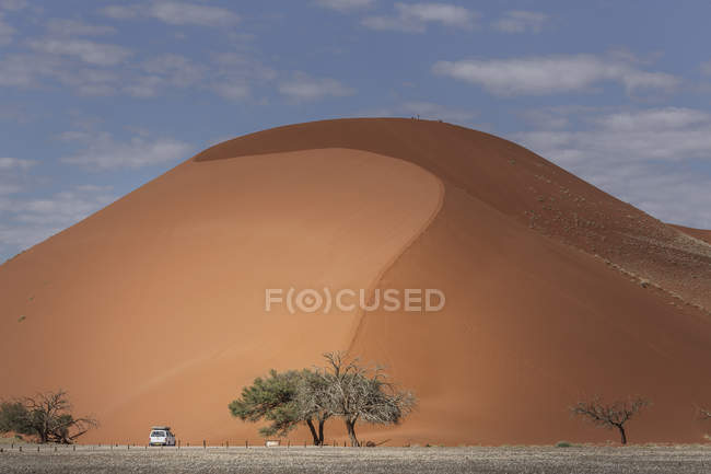 Camion a quattro ruote parcheggiato alla base di una duna di sabbia gigante, Parco Nazionale di Sossusvlei, Namibia — Foto stock
