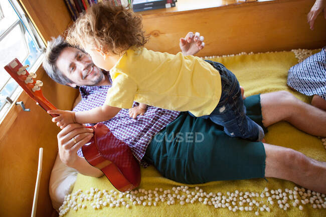 Father and son on bed in trailer home with guitar — Stock Photo