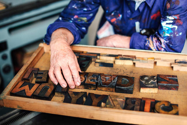 Senior craftsman reaching for wooden letterpress letters, mid section — Stock Photo