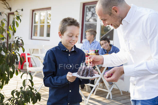 Mid adult man lighting sons birthday cake candles on patio — Stock Photo