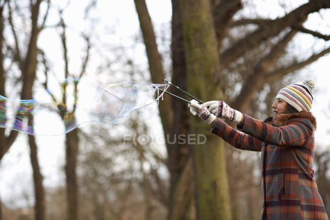 Mujer en el parque usando varita de burbujas para hacer burbujas - foto de stock
