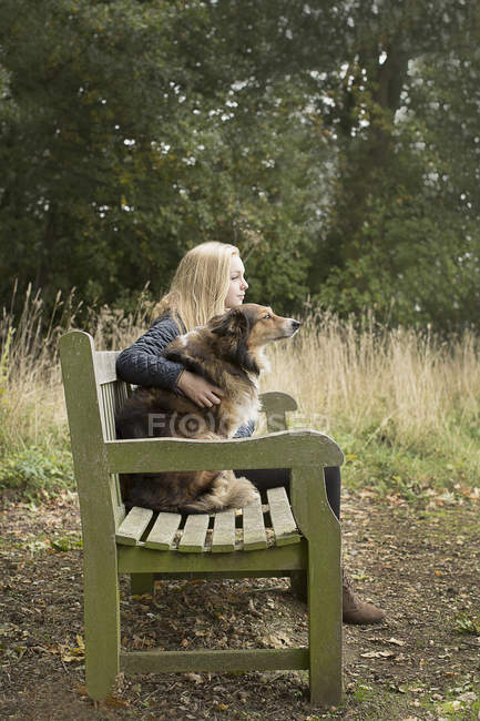 Adolescente sentada no banco de campo com o cão — Fotografia de Stock