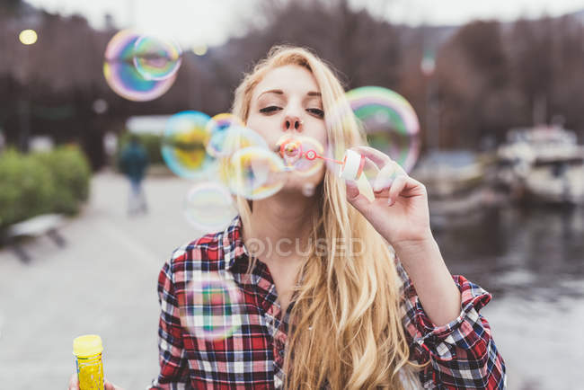 Portrait of young woman on waterfront blowing bubbles,  Lake Como, Italy — Stock Photo
