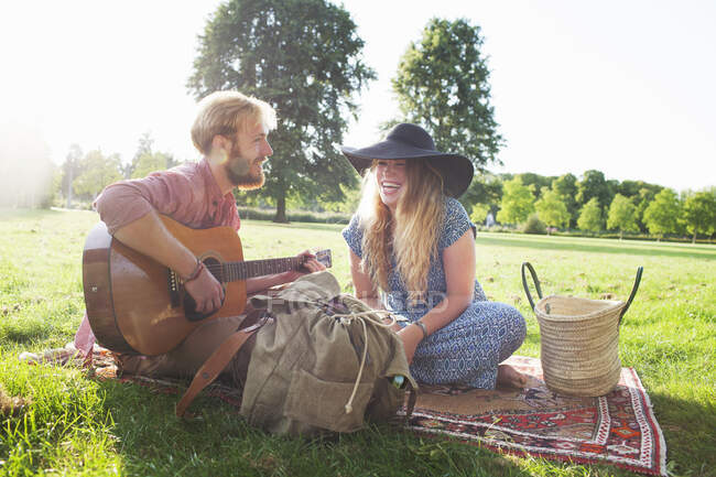 Romántica pareja joven tocando la guitarra acústica en el parque - foto de stock