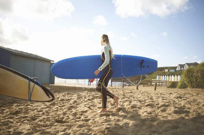 Femmina surfista sulla spiaggia, che trasporta tavola da surf — Foto stock