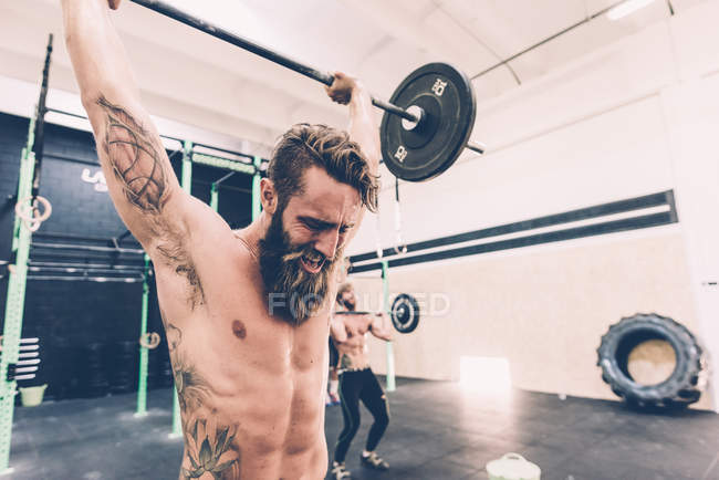 Young male cross trainer snatch lifting barbell in gym — Stock Photo
